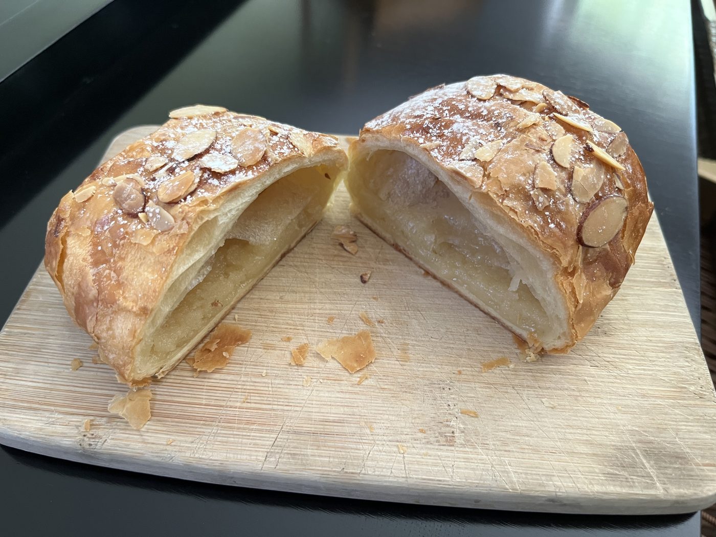 An almond croissant sliced open on a wooden cutting board
